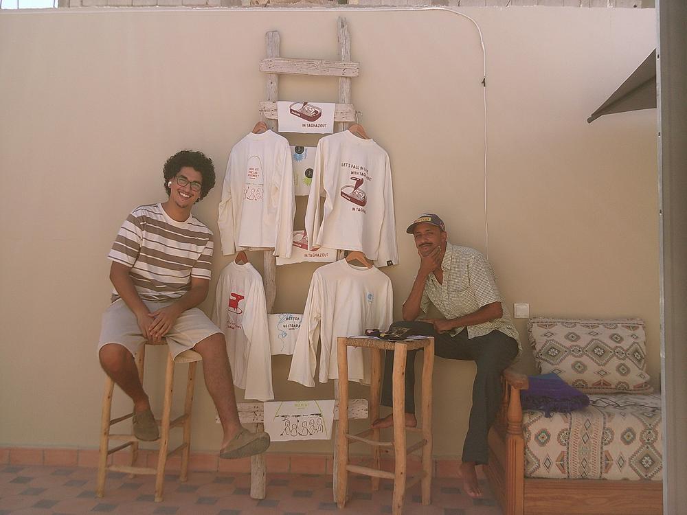 Deux amis assis devant une échelle où sont accrochés les tee-shirts