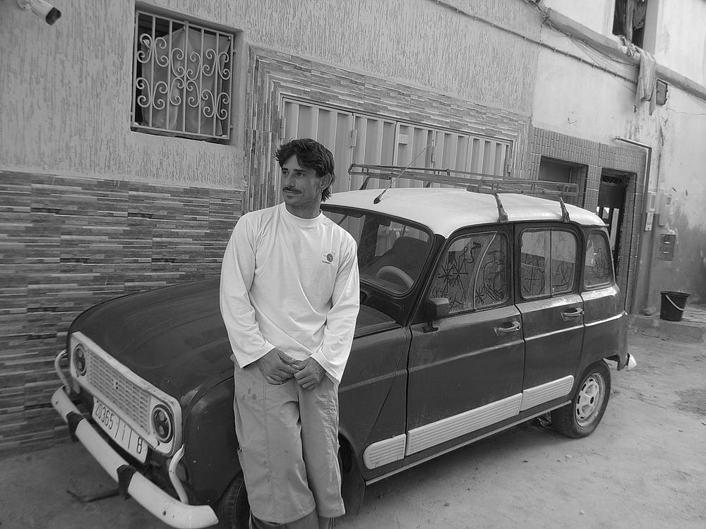 Homme adossé à une Renault 4, tee-shirt Saudade, en noir et blanc