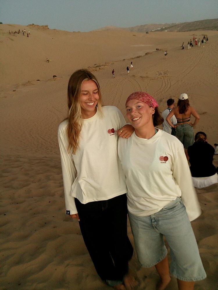 Deux amies en tee-shirt Saudade sur une dune au coucher du soleil