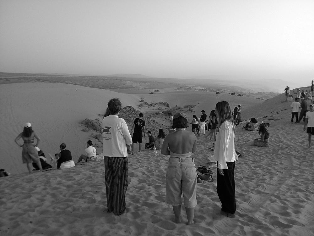 Foule assise sur les dunes au crépuscule, en noir et blanc