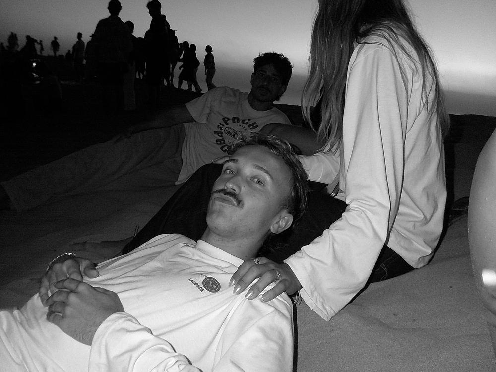 Portrait en noir et blanc, allongé dans le sable, tee-shirt Saudade
