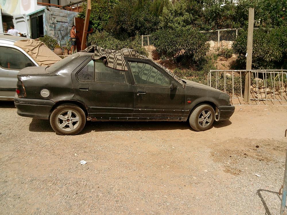 Vieille voiture noire garée sur un chemin de terre, une couverture sur le toit