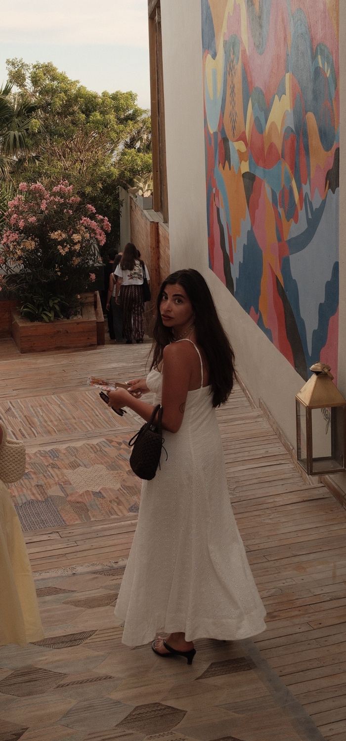 Nour, dans une robe blanche, se retourne devant une fresque colorée à Taghazout